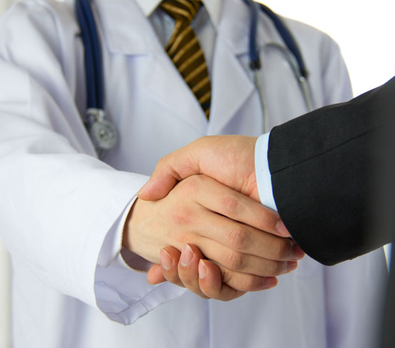 View of a handshake between an arm in a suit sleeve and a doctor in a white coat.