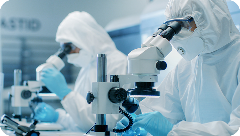 Two people in a lab in full protective gear looking through microscopes